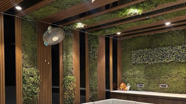 A modern reception area with a sectional sofa, vertical wooden slats, and a green wall with plants. - Hotel Elegant inn- Ichhapore (Surat)