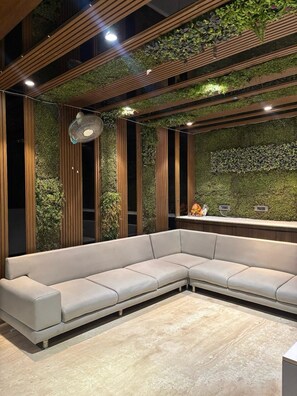 Un espace d’accueil moderne, doté d’un canapé modulable, de lambris en bois verticaux et d’un mur végétal.