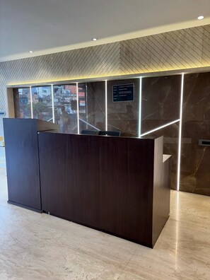 A reception desk with a dark wood finish, a glass partition, and a marble wall with a herringbone pattern. - Hotel Elegant inn- Ichhapore (Surat)