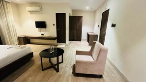 A hotel room with a bed, a sofa, a small table, a TV, and a wardrobe. - Hotel Elegant inn- Ichhapore (Surat)