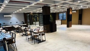 A spacious indoor area with multiple tables and chairs, a tiled floor, and a modern ceiling design with recessed lighting. - Hotel Elegant inn- Ichhapore (Surat)