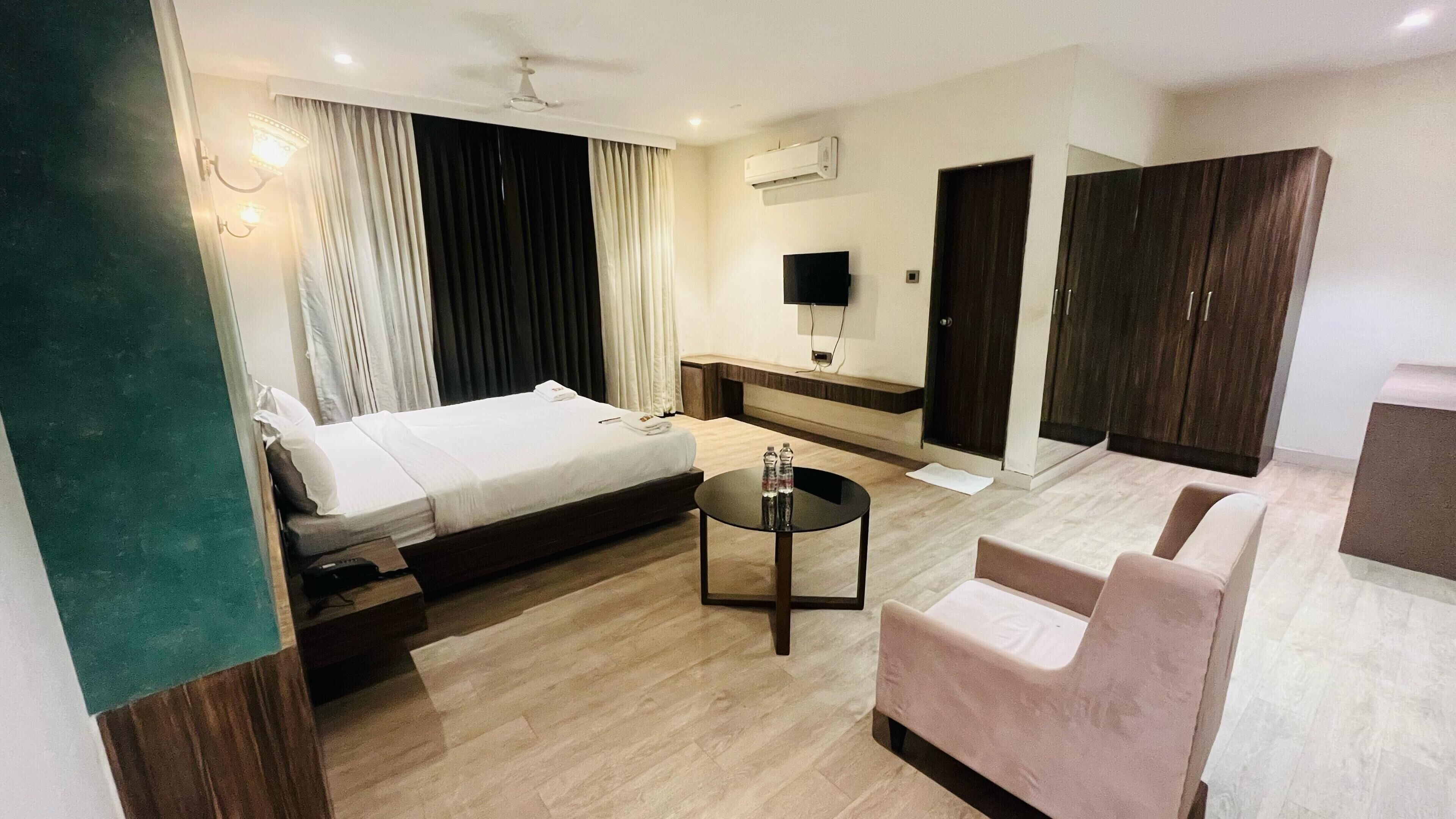 A hotel room with a bed, a small table, a sofa, a TV, and a wardrobe.