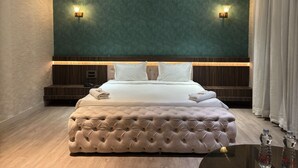 A modern hotel room with a large bed, a tufted headboard, and two wall-mounted lights. - Hotel Elegant inn- Ichhapore (Surat)
