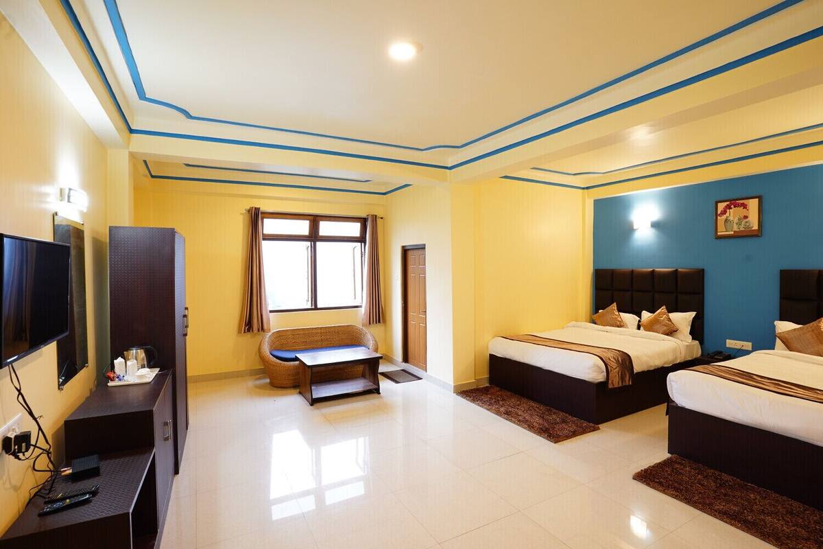 A hotel room with two beds, a sofa, a TV, and a window with curtains.