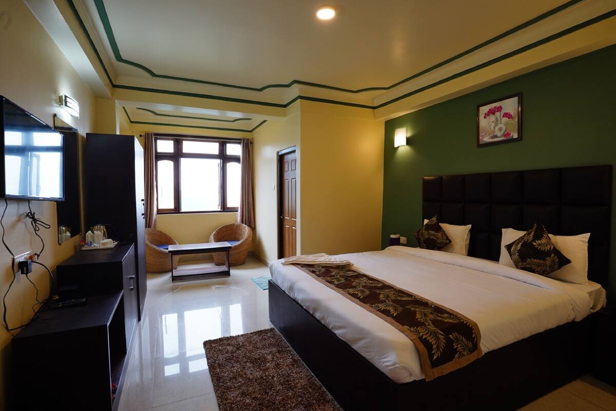 A hotel room with a large bed, a desk with a chair, a television, and a window with curtains.