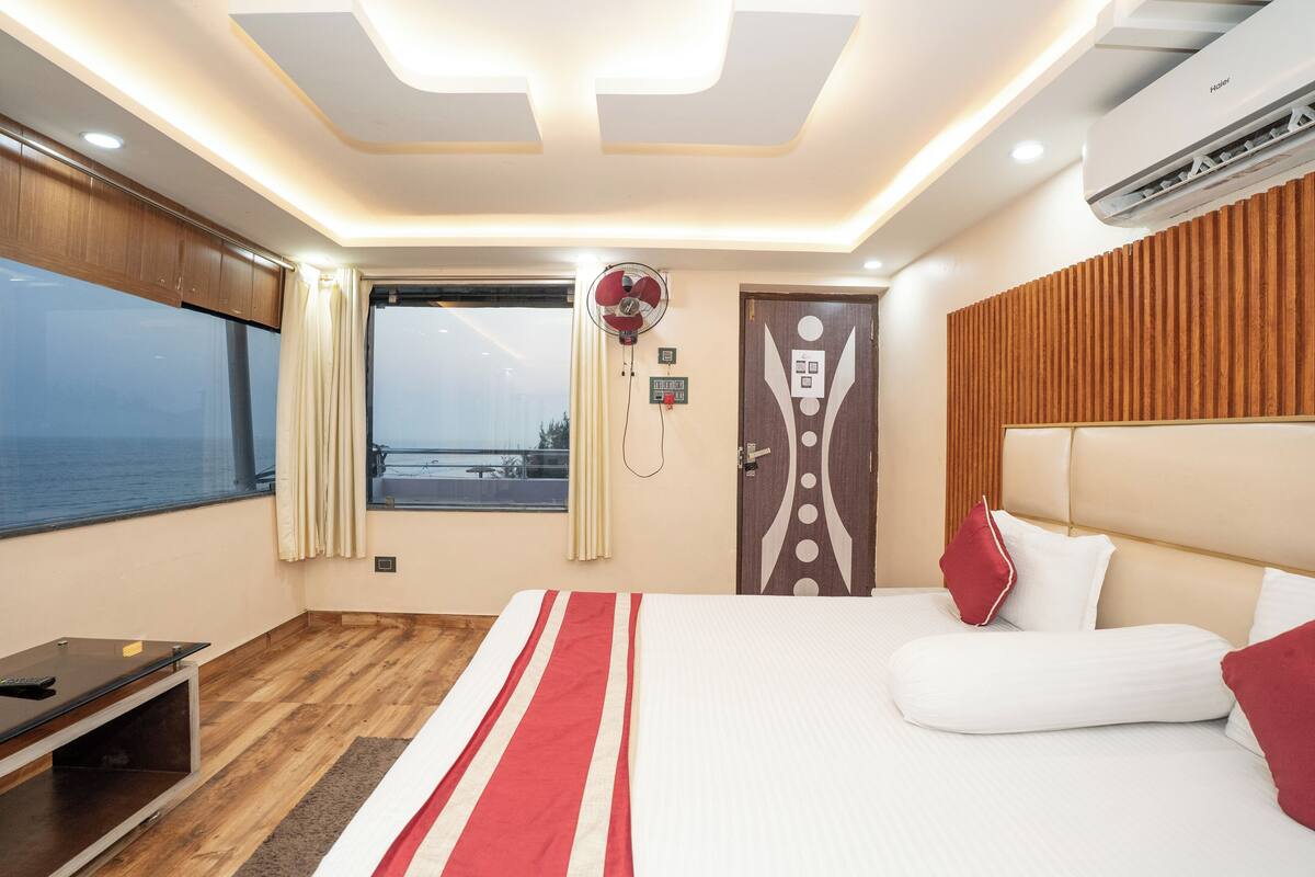 A modern hotel room with a large bed, a desk, and a view of the sea.