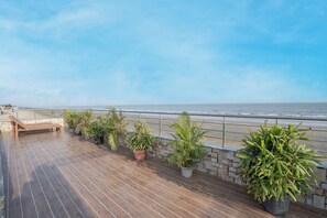 En træterrasse med bænk og plantekasser, med udsigt over en strand og et hav.