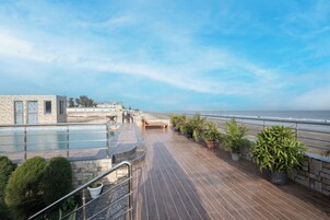 A wooden deck with potted plants, a pool, and a view of the ocean.