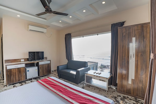 A hotel room with a bed, a desk with a television, a chair, a small table, and a view of the ocean. - Mandarmani Kiss of Sea Resort (Kanthi)