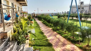 A pathway lined with greenery, a swing set, and hanging decorations.