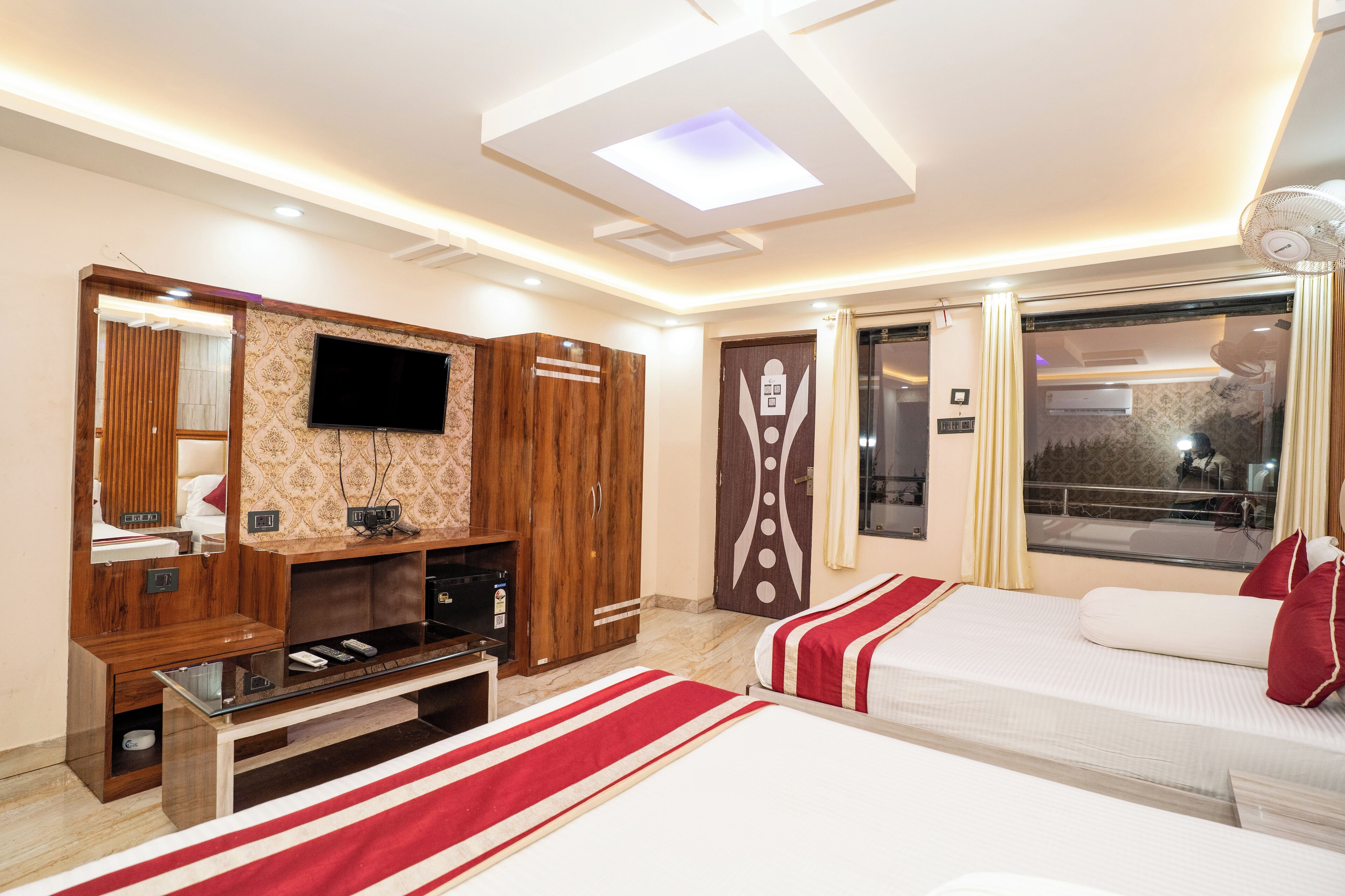 A hotel room with two beds, a TV, a wardrobe, and a window with curtains.