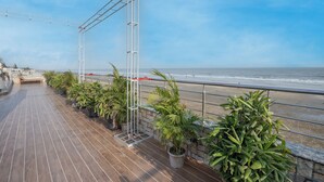 A wooden deck with potted plants, a metal railing, and a view of the ocean.