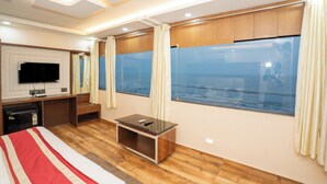 A modern hotel room with a large window, wooden flooring, a flat-screen TV, a desk, and a bed with striped bedding.