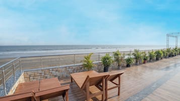A wooden deck with tables and chairs overlooking a beach.