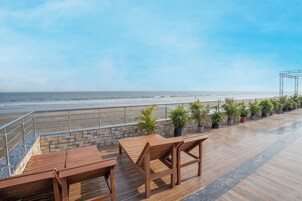 A wooden deck with tables and chairs overlooking a beach.