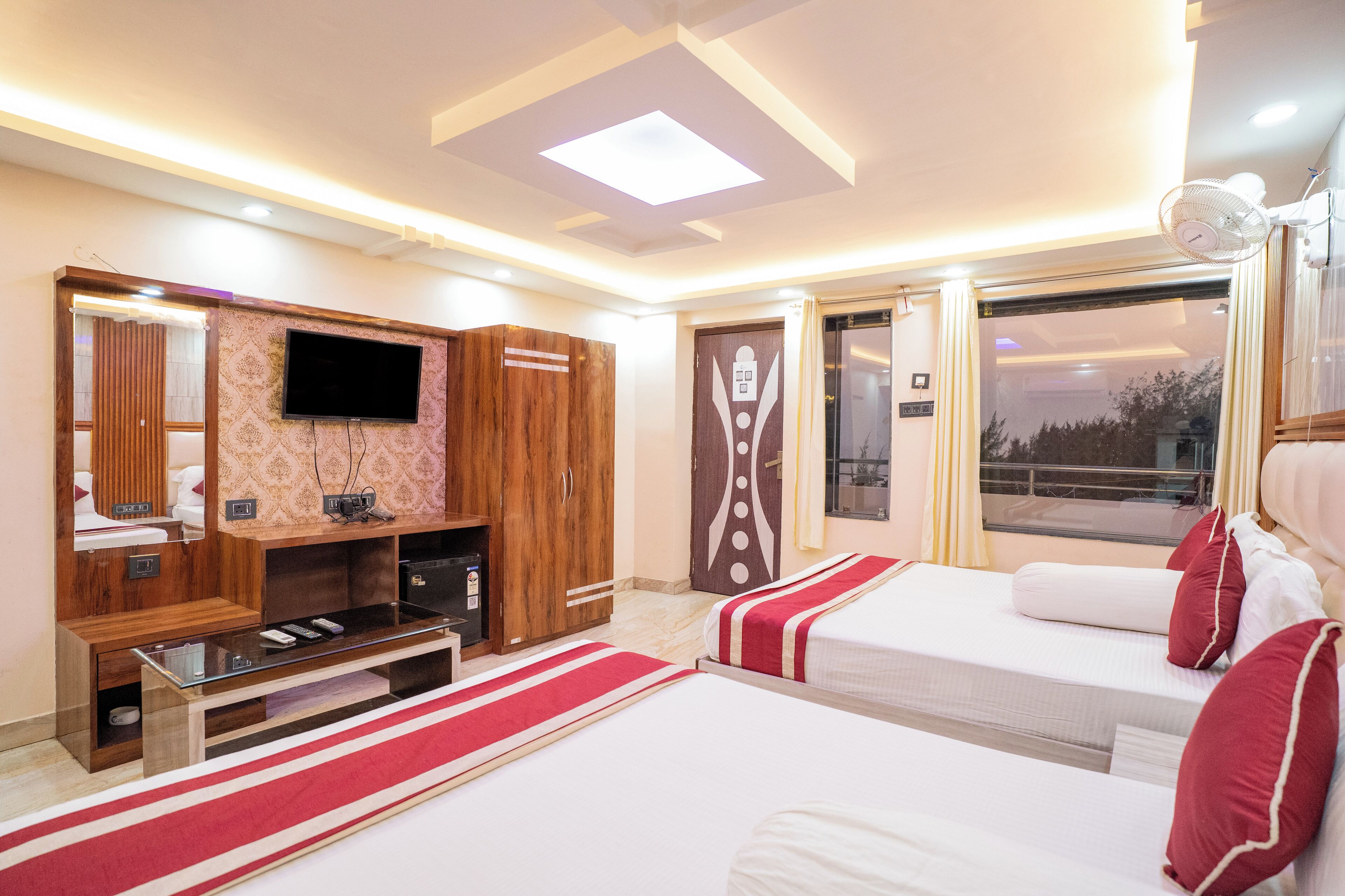 A hotel room with two beds, a TV, a wooden wardrobe, and a window with curtains.