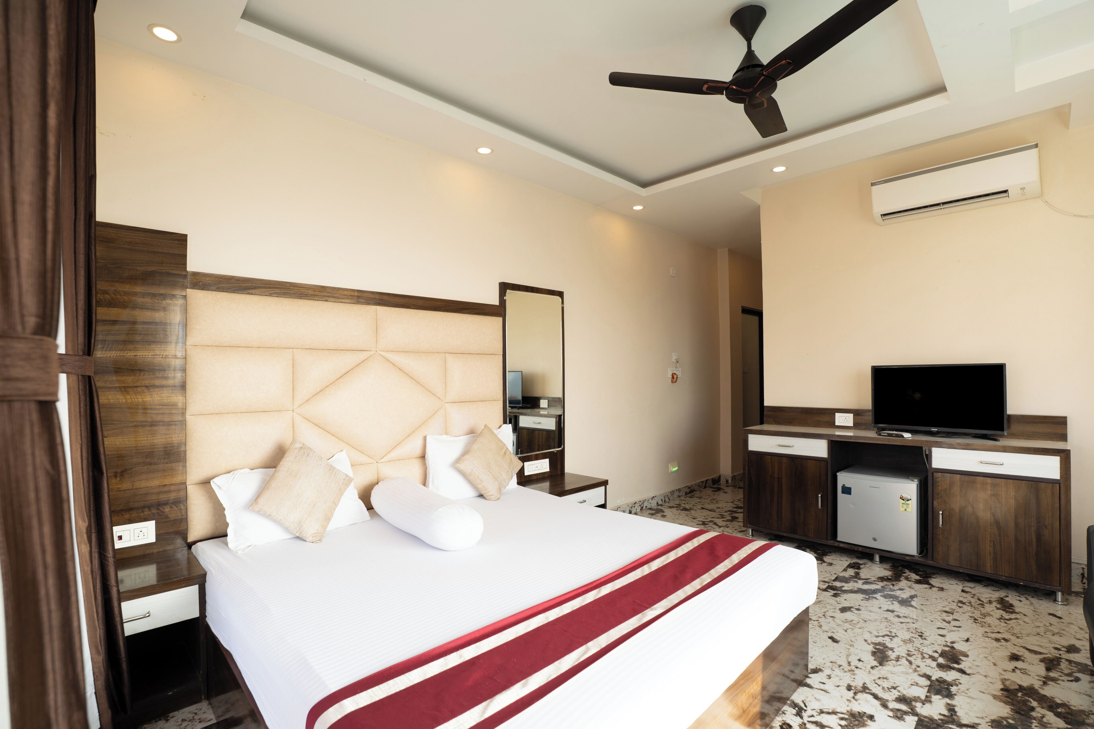 A hotel room with a bed, a desk, a television, and an air conditioning unit.