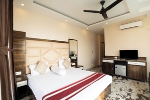 A hotel room with a bed, a desk, a television, and an air conditioning unit.