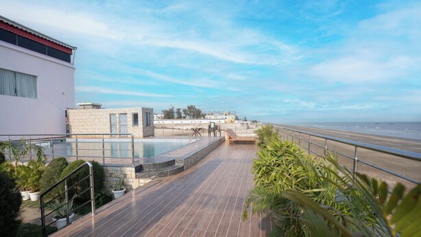 A rooftop pool area with a view of the beach, a stone structure, and potted plants.