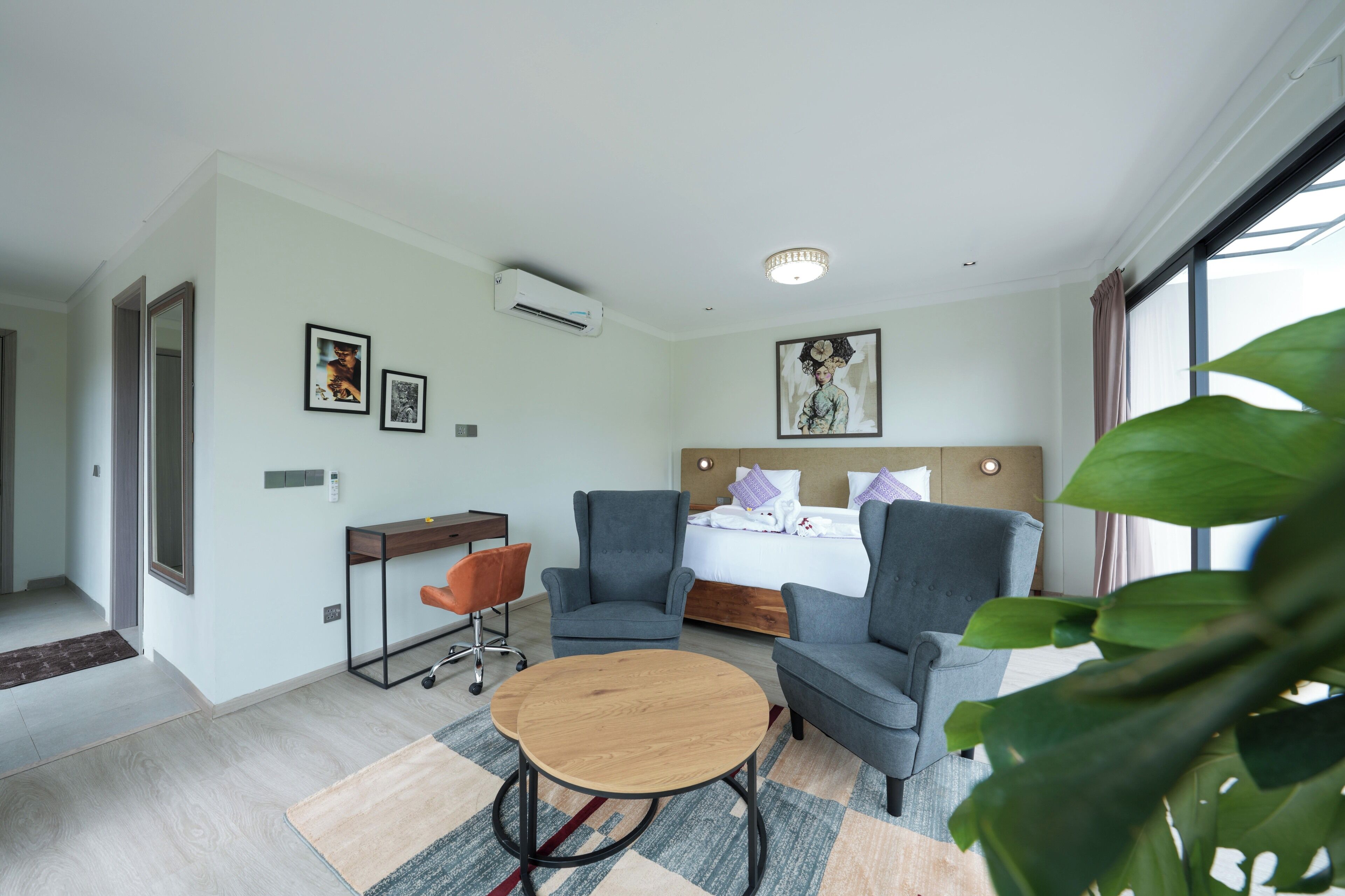 A modern hotel room with a bed, two armchairs, a small table, and a desk.