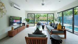 Una sala de estar moderna con televisor, asientos y vista a una piscina.