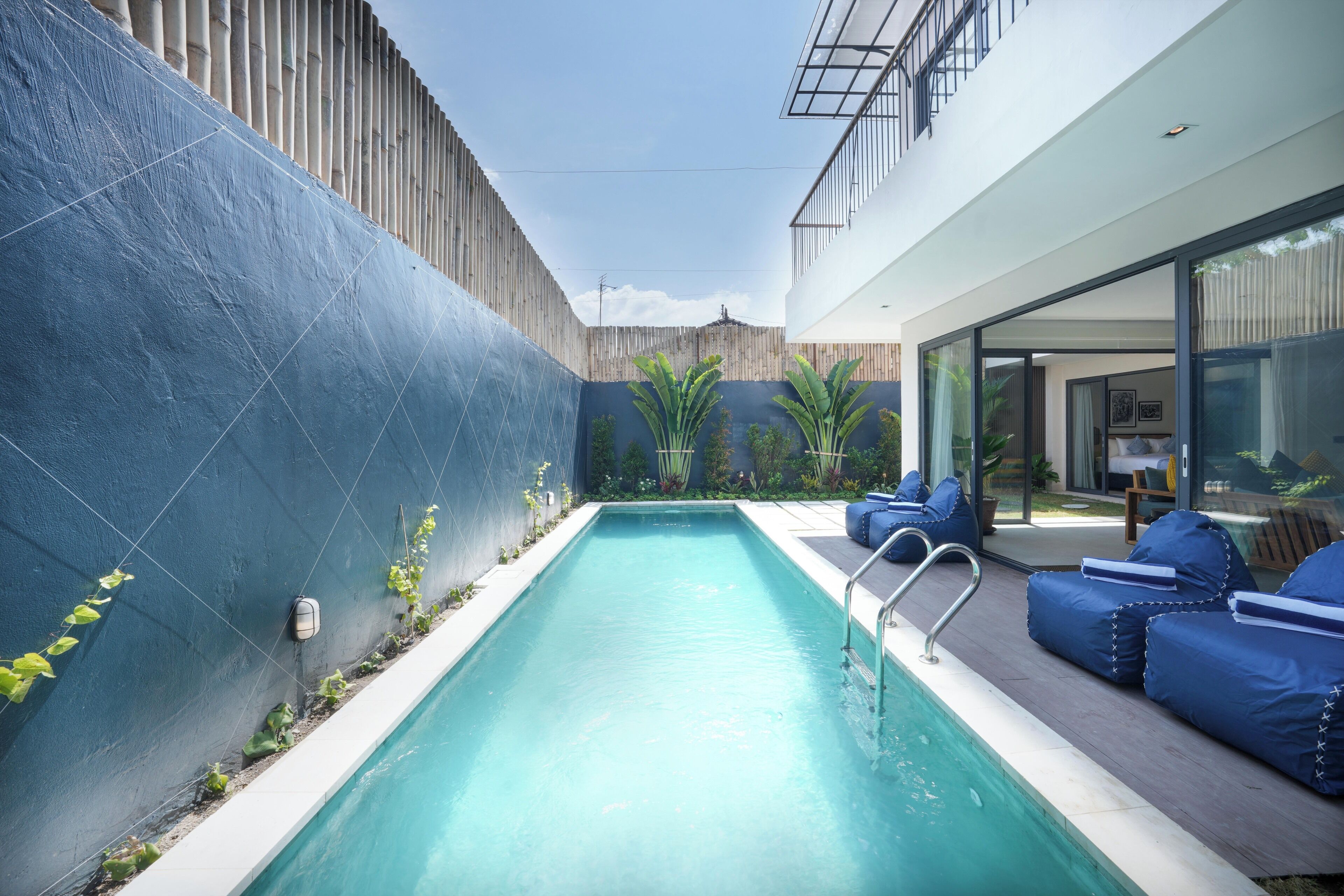 A modern outdoor pool area with a blue-tiled wall, seating, and a view of the adjacent building.