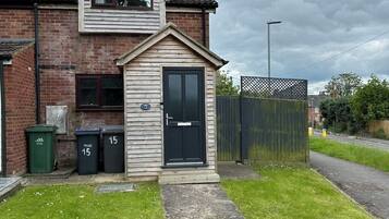 A two-story house with a small front porch, a mailbox, and two trash bins.