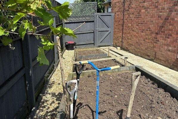 A garden bed with a blue hose, a shovel, and a wheelbarrow.