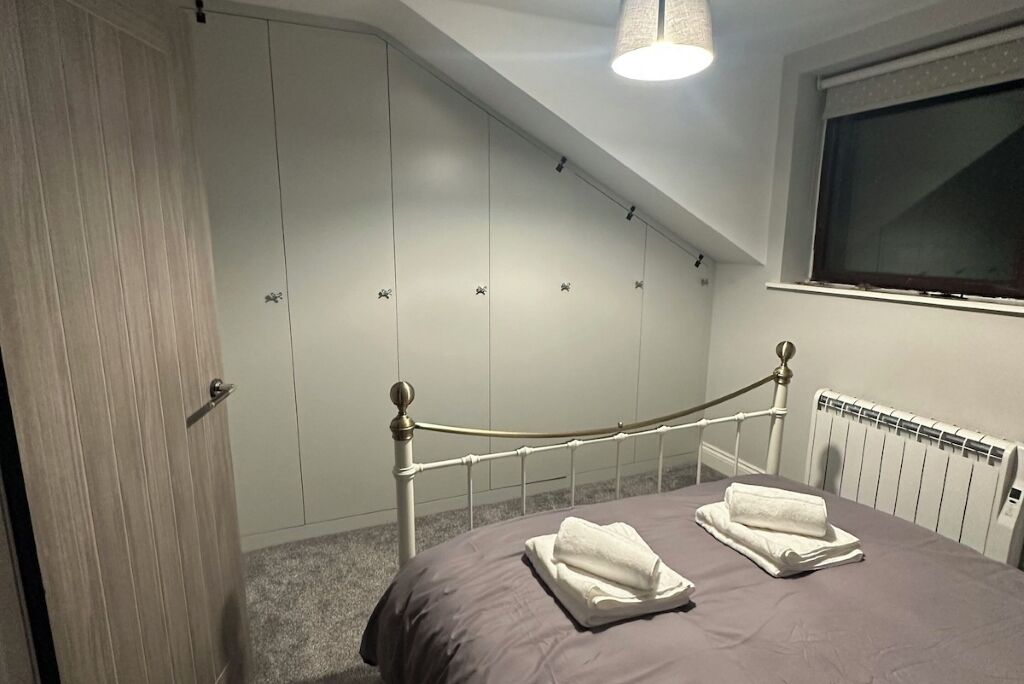 A bedroom with a bed, a radiator, a window, and a wardrobe.