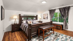 A bedroom with a bed, bedside tables, a bench, a window with curtains, and a patterned rug. - Wonderful Forested Retreat, Hot Tub, Pet Friendly, Game Room, Pool Table, Fire-Pit, on 2 Acres (Gresham)