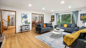 A modern living room with two sofas, a coffee table, and a dining area with chairs and a table. - Wonderful Forested Retreat, Hot Tub, Pet Friendly, Game Room, Pool Table, Fire-Pit, on 2 Acres (Gresham)