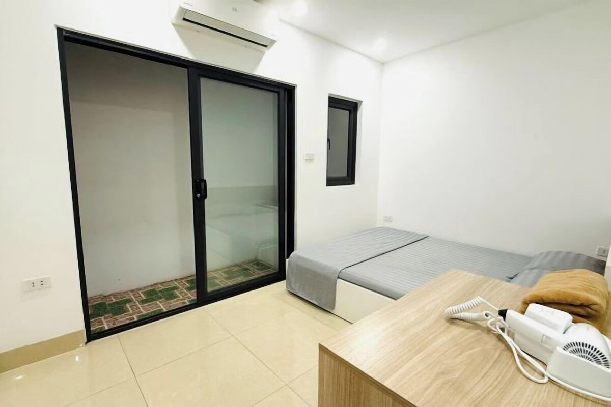 A room with a bed, a desk with a hairdryer, a sliding door, and a small window.