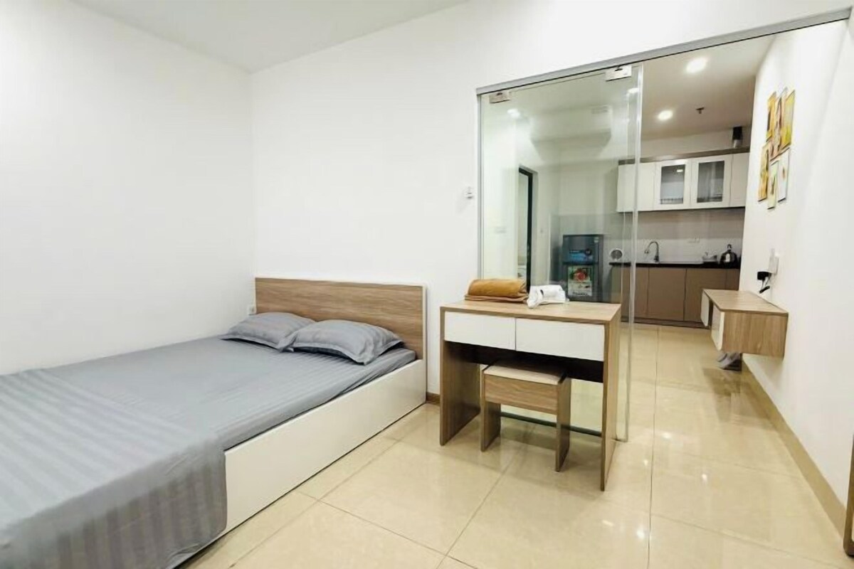 Una habitación pequeña con cama, escritorio y una kitchenette al fondo.