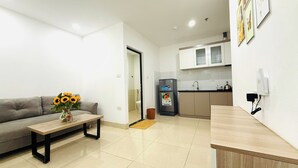 A modern apartment with a grey sofa, a wooden coffee table, a kitchen with white cabinets, and a refrigerator. - Era Apartment Dinh Thon (Hanoi)