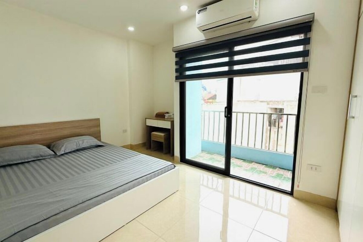 A bedroom with a bed, a desk, and a sliding glass door to a balcony.