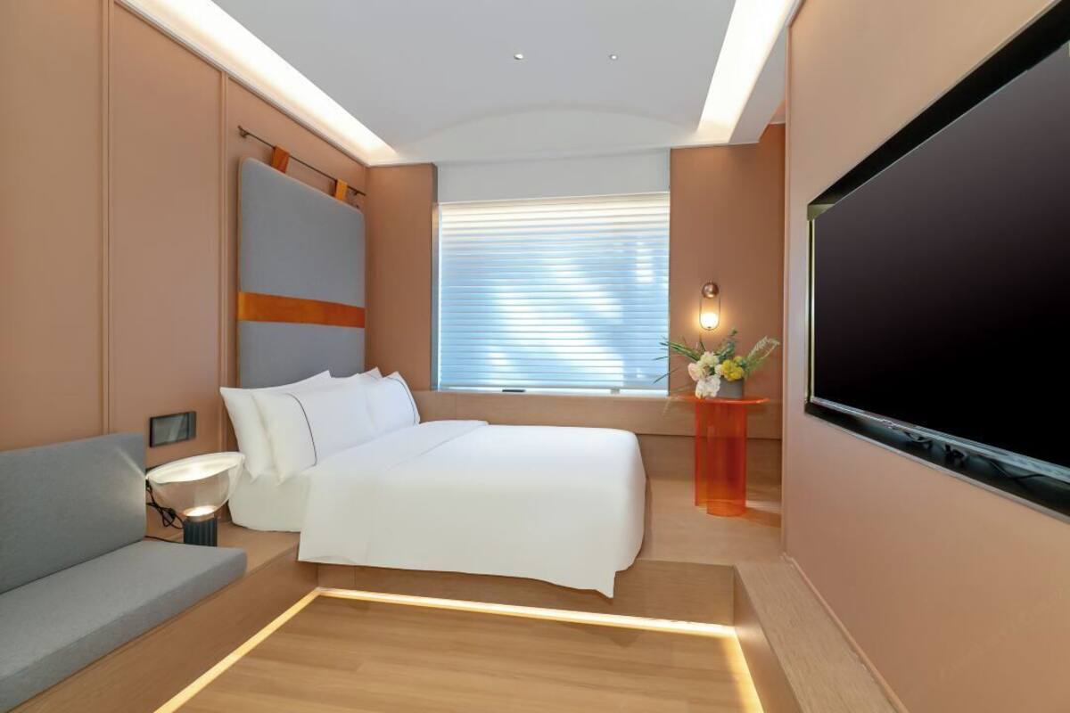 Habitación de hotel moderna con cama, sofá, televisión y ventana con persianas.