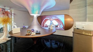 Eine moderne Lobby mit einer einzigartigen, großen, trichterförmigen Leuchte, einem Empfangsbereich und einem großen Bildschirm, der einen Zimmer zeigt.