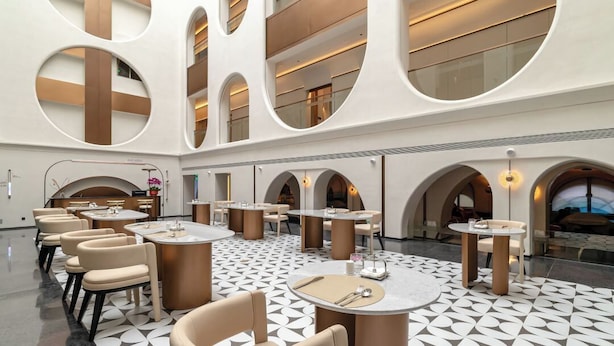 Eine moderne Hotelhalle mit runden Tischen, bequemen Sitzgelegenheiten und einem geometrisch gemusterten Boden.