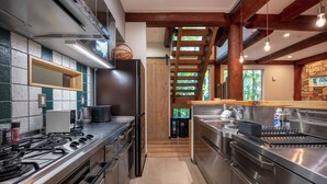 A modern kitchen with stainless steel appliances, a wooden staircase, and a view of the outdoors. - Chise Fukuro by H2 Life (Furano)