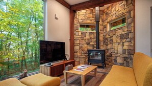 A cozy living room with a stone fireplace, a large TV, and comfortable seating. - Chise Fukuro by H2 Life (Furano)
