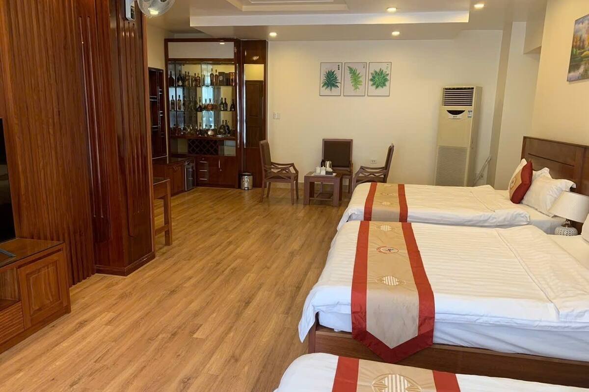 A hotel room with two beds, a wooden floor, a minibar, and a seating area with chairs.