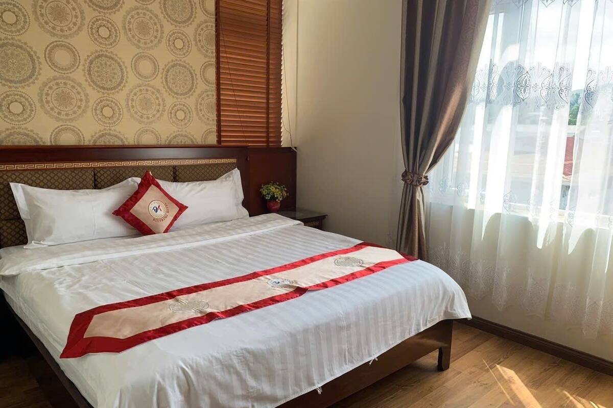 A neatly made bed with a white and red bedspread, a wooden headboard, and a nightstand with a plant.