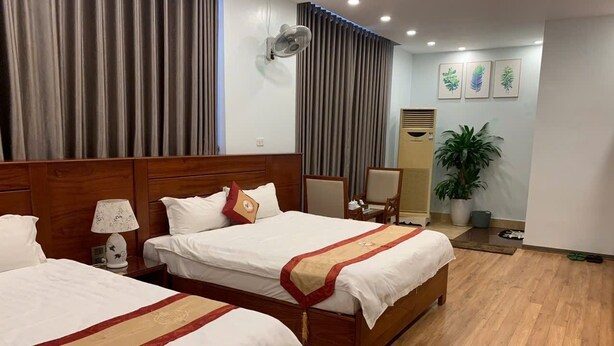 A hotel room with two beds, a desk, a chair, a potted plant, and a wall-mounted fan. - Duc Trung Hotel CB by Bayluxury (Thuc Phan)