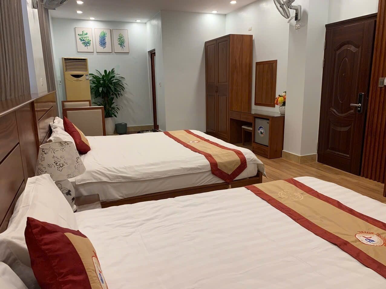 Una habitación de hotel con dos camas, un armario, un escritorio y una planta en maceta.