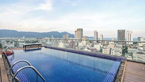 Une piscine à débordement située sur le toit, offrant une vue sur la ville, avec des gratte-ciel et des montagnes en arrière-plan.