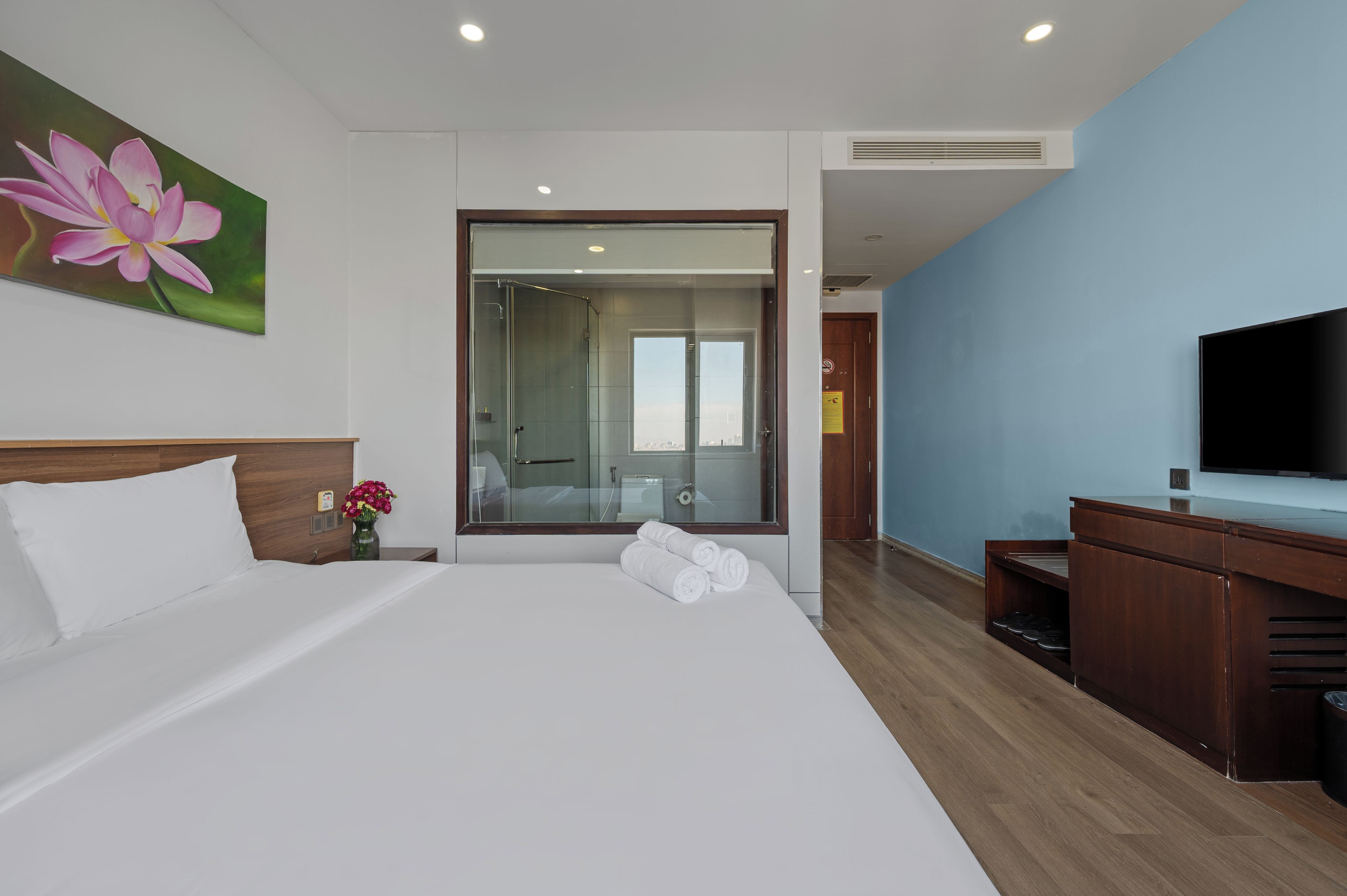 Una habitación de hotel con una cama grande, televisión, cómoda de madera y cabina de ducha de vidrio.