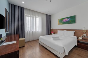 A hotel room with a bed, a desk, a chair, a bedside table with a lamp, a painting, and a telephone. - My Khe Diamond Beach Hotel (Da Nang)