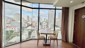 Une pièce d’angle avec une grande fenêtre, une table en bois, deux chaises et une vue sur le paysage urbain.