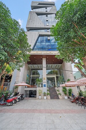 L’entrée d’un hôtel au design moderne, caractérisée par une façade en verre, un espace d’entrée abrité et un escalier menant au hall d’accueil.
