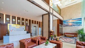 Un hall d’hôtel avec des canapés en cuir, un comptoir d’accueil et un grand tableau représentant une scène de plage.